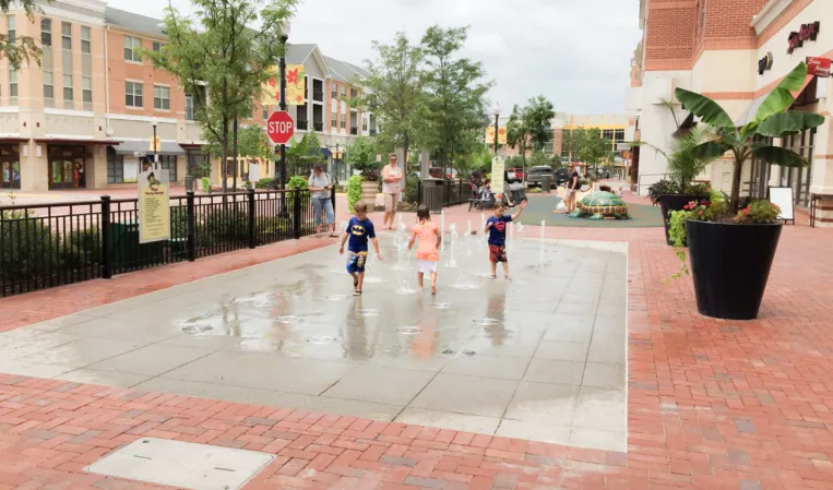 Interactive fountain with water jets along a pedestrian walkway in an outdoor shopping plaza