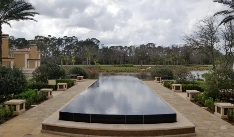 Long rectangular reflecting pool with dark stone edges in a landscaped garden