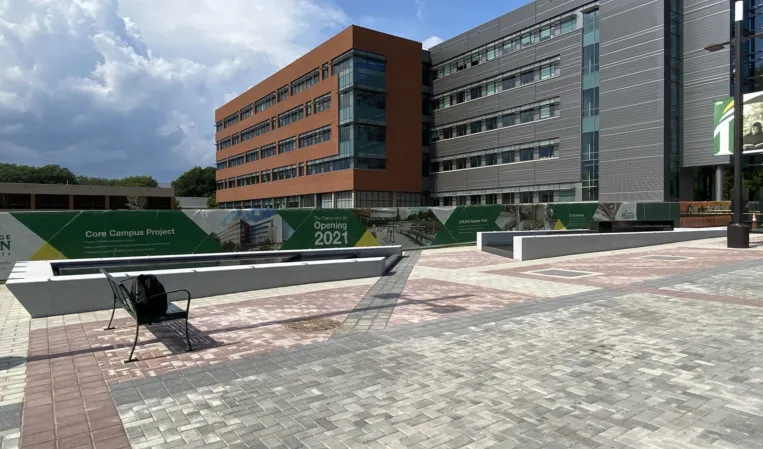 Modern university campus with a paved plaza, landscaped lawns and a rectangular reflecting pool