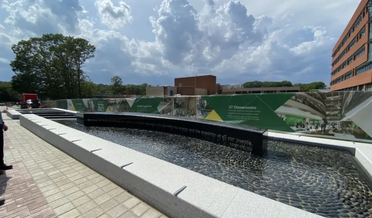 Long granite reflecting pool with dark water and cascading edges on a modern university campus