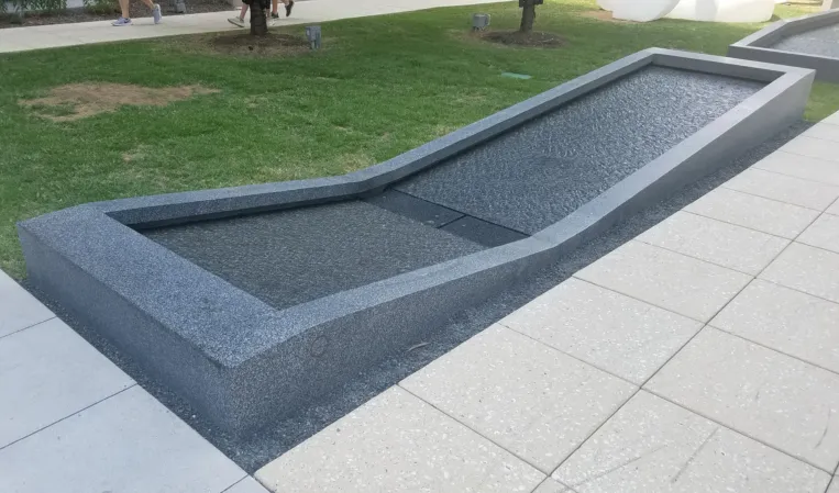 Long, narrow granite fountain basin with a sloped design beside a landscaped lawn