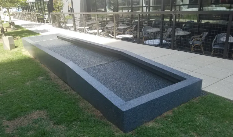 Long, narrow granite fountain basin with a sloped design beside a landscaped lawn