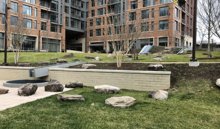 Landscaped courtyard with stone water features, rocks and trees in front of a modern residential building
