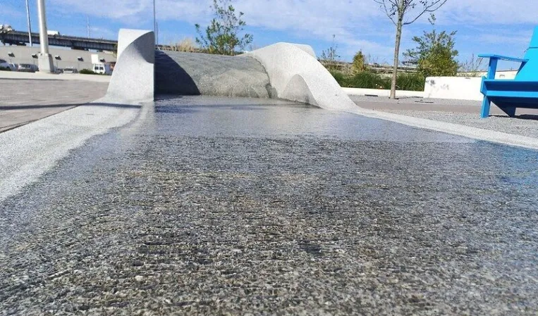 Close-up of a granite water feature with a sloped overflow edge and shallow basin beside a landscaped garden