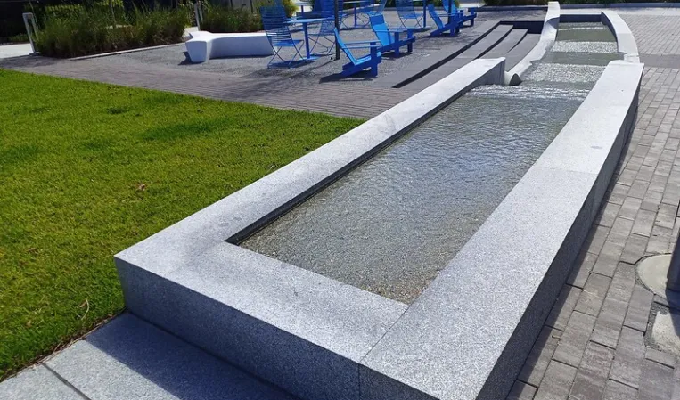 Long granite water channel with cascading sections beside a landscaped outdoor seating area