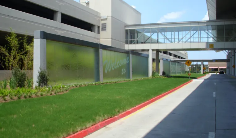 Large glass water wall beside a landscaped lawn and modern office buildings