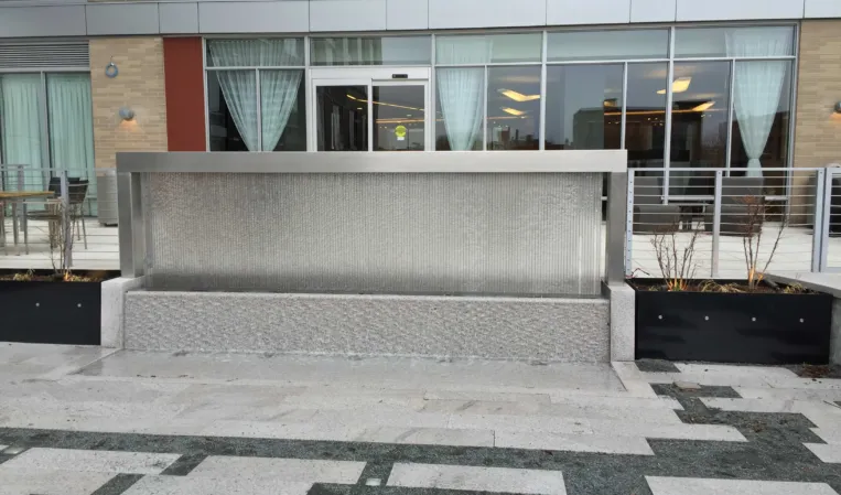Rectangular granite water wall with cascading water in front of a modern building