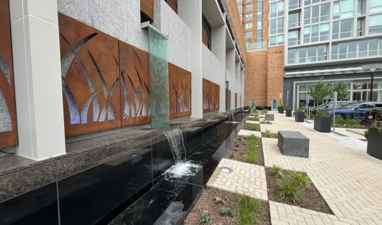 Granite water wall with cascading spouts and decorative metal panels in a modern courtyard