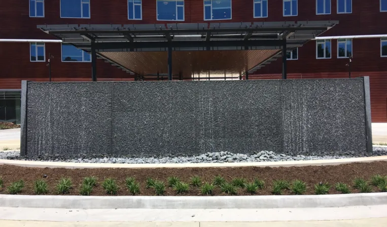 Large granite water wall with cascading water in front of a brick building