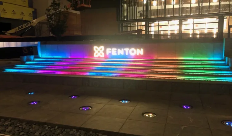 Colorfully illuminated stepped fountain with Fenton signage at night