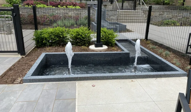 Rectangular granite fountain with two vertical water jets in a landscaped courtyard