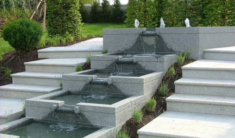 Multi-level cascading granite fountain with stepped basins and integrated water features in a landscaped garden