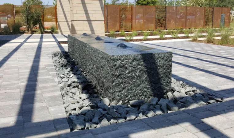 Rectangular granite fountain with a polished surface surrounded by decorative stones in a landscaped courtyard