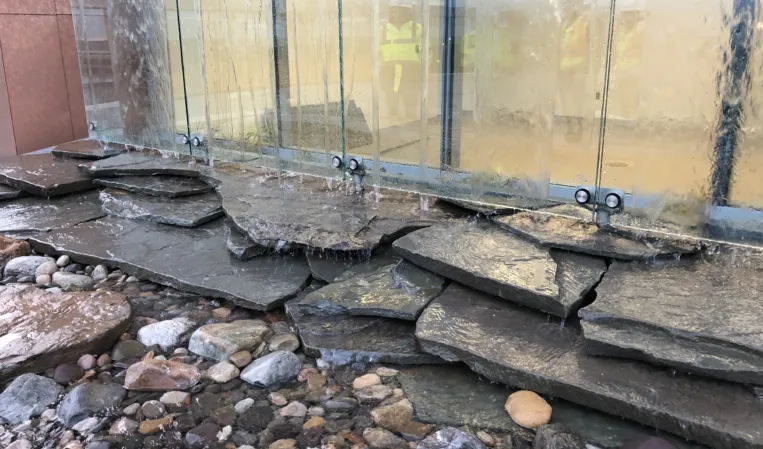 Natural stone water feature with layered slate slabs, river pebbles and a glass water wall