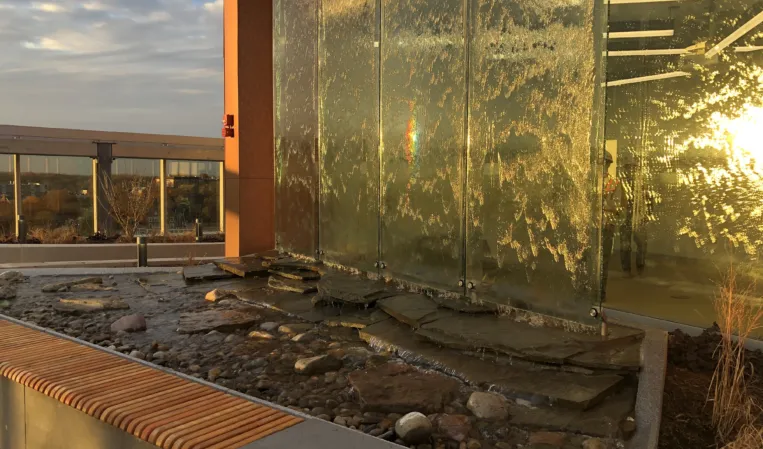 Natural stone water feature with layered slate slabs, river pebbles and a glass water wall at sunset