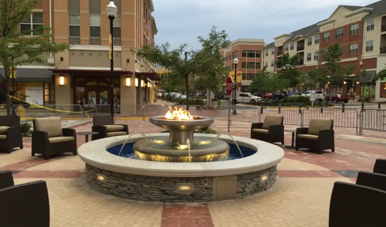 Circular stone fountain with a central fire feature surrounded by outdoor seating in an urban plaza