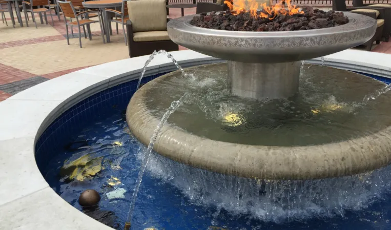 Circular stone fountain with a central fire feature surrounded by outdoor seating in an urban plaza