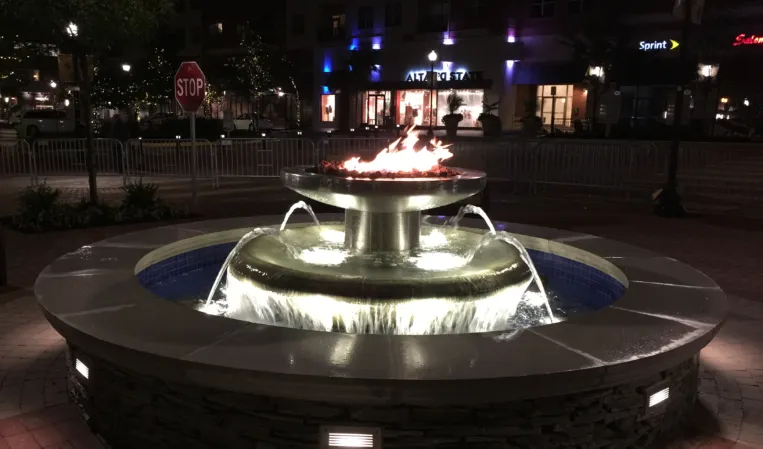 Illuminated circular stone fountain with cascading water and a central fire feature at night