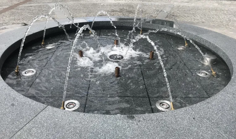 Circular granite fountain with arched water jets spraying into a shallow basin