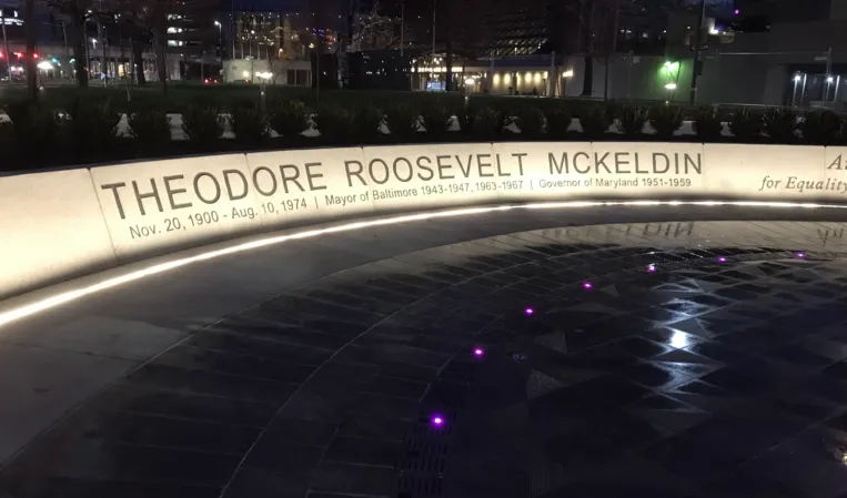 Illuminated curved memorial wall honoring Theodore Roosevelt McKeldin with embedded colored lights in the fountain plaza at night