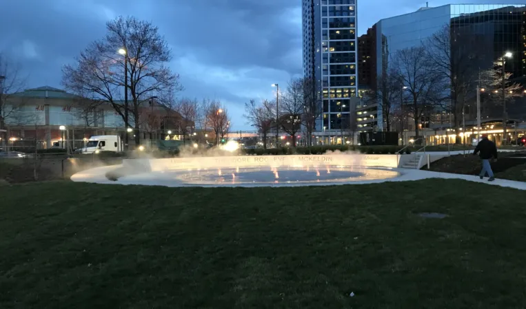 Illuminated interactive fog fountain with programmable water jets and mist effects in an urban plaza at dusk