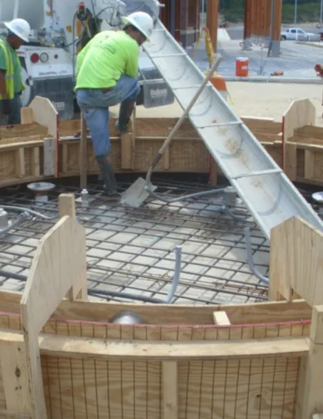 Worker pouring concrete into a reinforced foundation formwork at a construction site