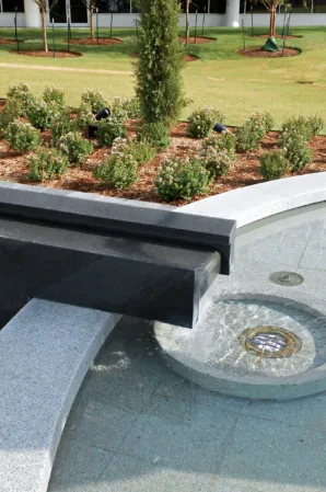 Close-up of a granite fountain with an integrated water channel and circular drain beside a landscaped garden