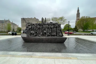 Bronze sculpture depicting a group of people on a granite pedestal surrounded by a shallow reflecting pool