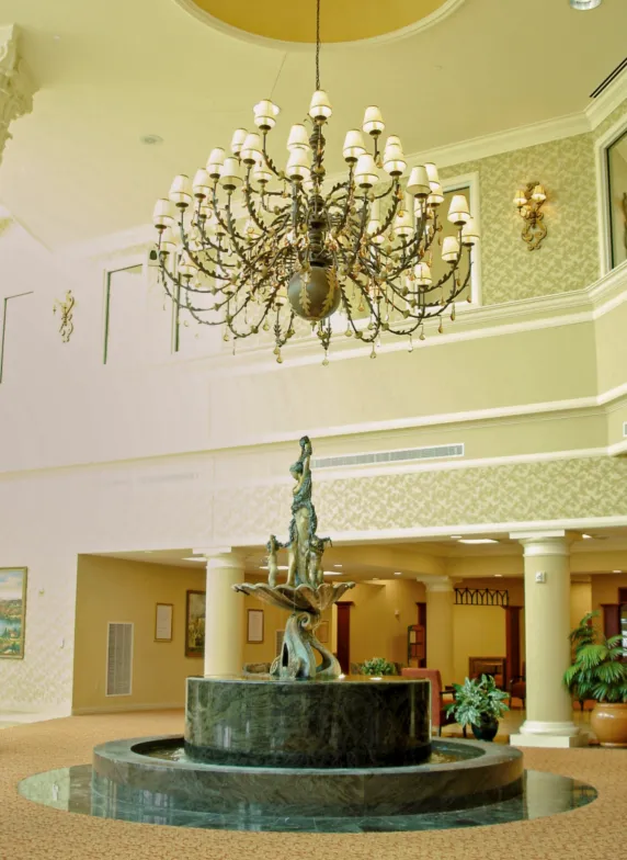 Indoor fountain with a bronze sculpture and circular granite basin beneath an ornate chandelier