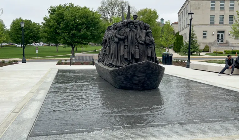 Reflecting pool at sculpture base — water flows around the base so the bronze boat appears to be moving or sailing forward