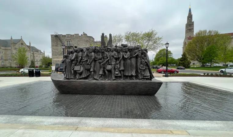 Bronze sculpture depicting a group of people on a granite pedestal surrounded by a shallow reflecting pool