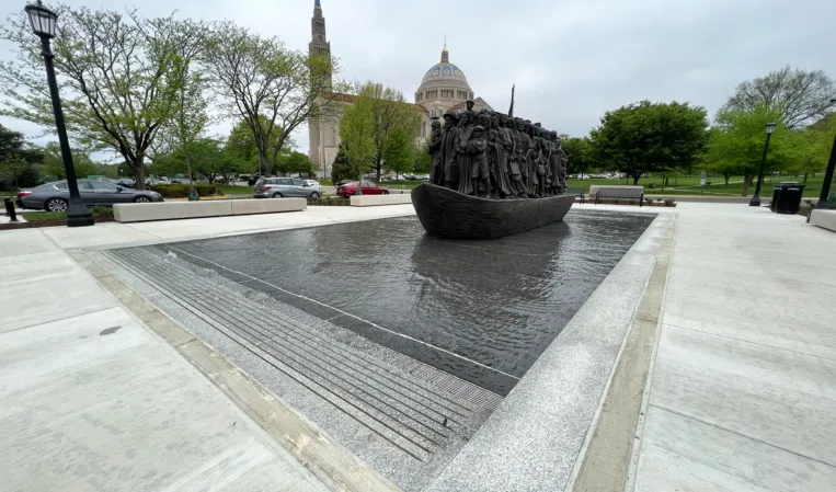 Reflecting pool at sculpture base — water flows around the base so the bronze boat appears to be moving or sailing forward
