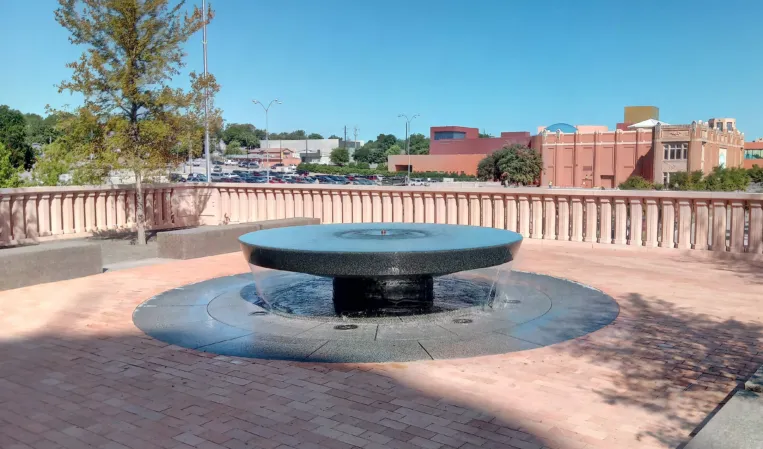 Circular granite fountain with a raised disc-shaped basin on a brick-paved terrace
