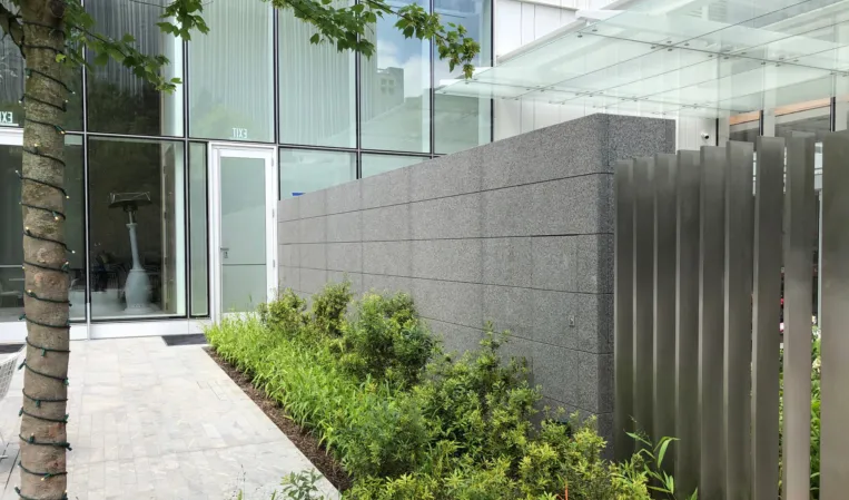 Grey granite wall surrounded by greenery beside a modern glass building