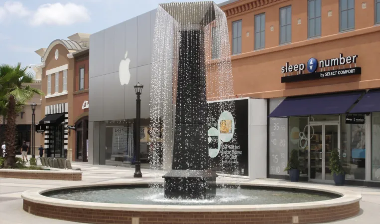 Tall rectangular fountain with cascading water flowing into a circular basin in an outdoor shopping plaza