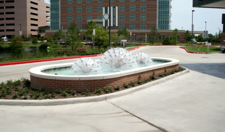 Oval fountain with two decorative spherical water features outside a modern hospital building