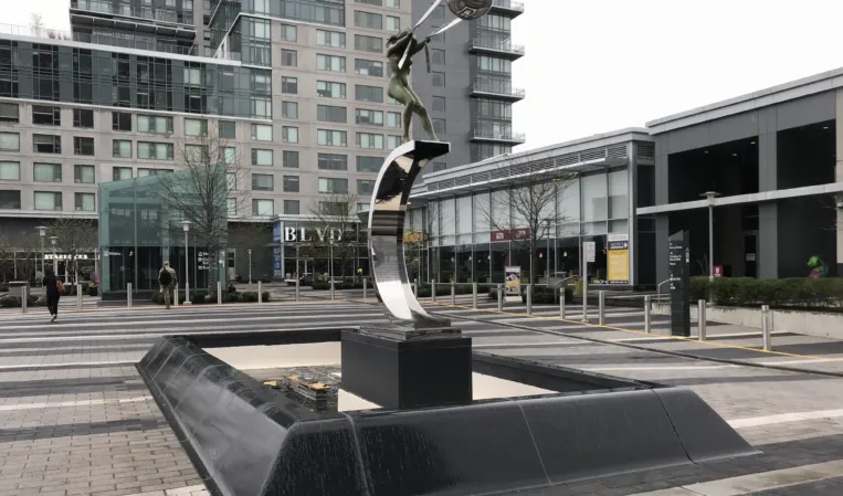 Abstract metal sculpture above a rectangular black granite fountain in a modern urban plaza
