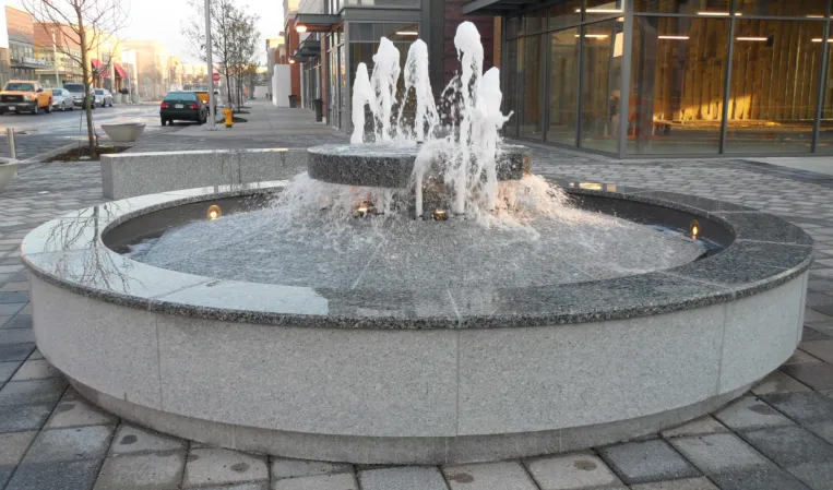 Circular granite fountain with multiple water jets cascading into a lower basin in an urban plaza