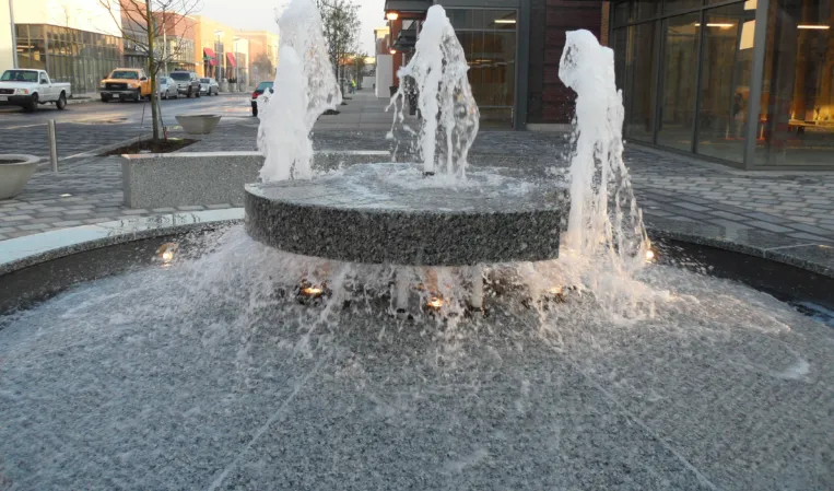 Circular granite fountain with multiple water jets cascading into a lower basin in an urban plaza